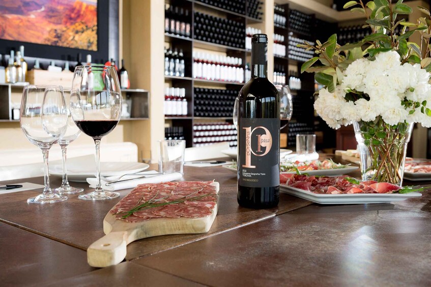 A wine bottle, glasses, a plate of food, and a flower arrangement on a table. 5