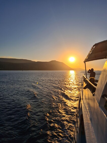 Un atardecer sobre aguas tranquilas, con un barco y gente en la cubierta. 3