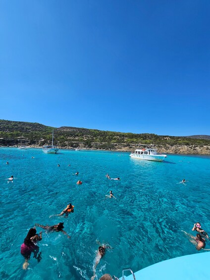 Mar azul cristalina con gente nadando y un barco anclado cerca de la orilla. 5