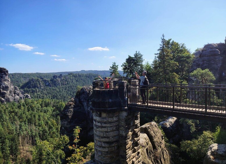A stone bridge with people on it, overlooking a forested valley. 4