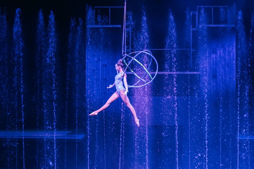 A performer in a blue costume executing a water fountain act with a hoop. 2