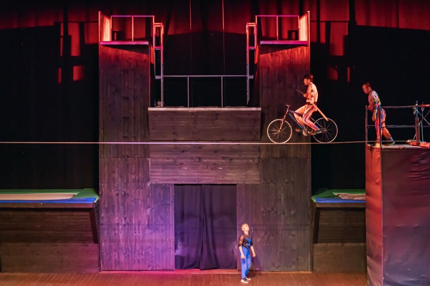 A stage with a wooden structure, a person on a bicycle, and another person standing on a platform. 3