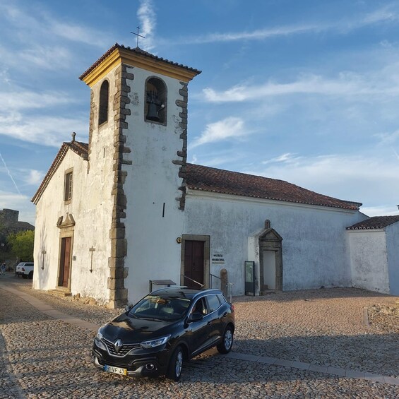 A white church with a bell tower, a black car parked in front, and a sign for the Museu Municipal. 4