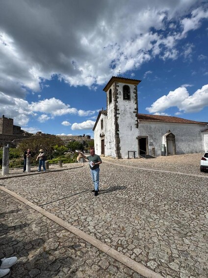 A historic church with a bell tower, cobblestone plaza, and visitors. 1