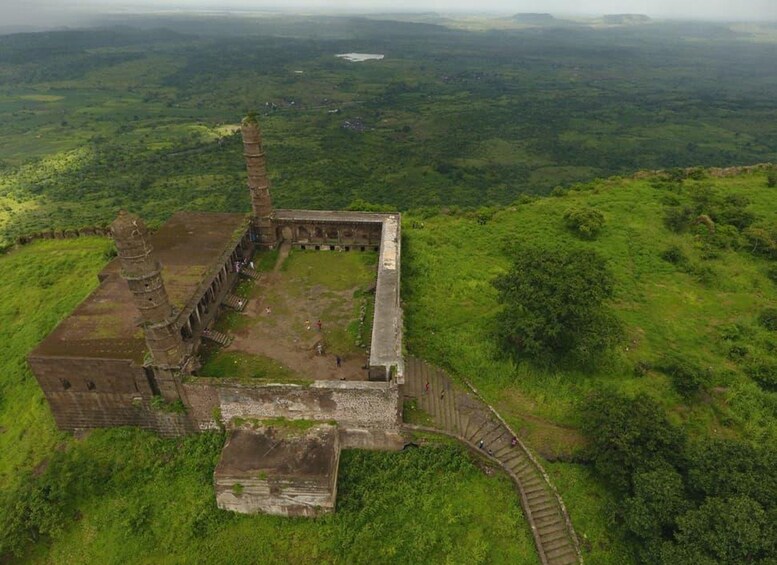 An ancient stone structure with a spiral staircase, surrounded by lush green hills. 1