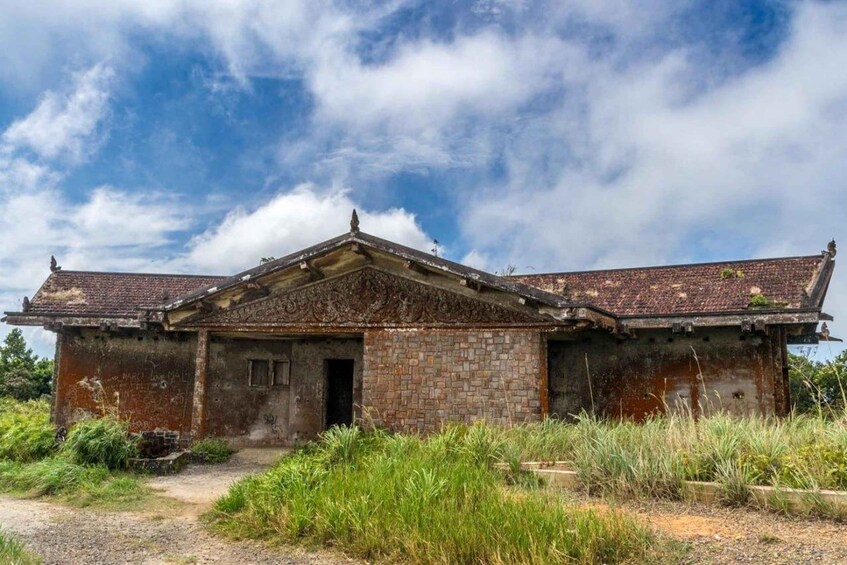 An abandoned building with a tiled roof and brick walls, surrounded by overgrown vegetation. 2