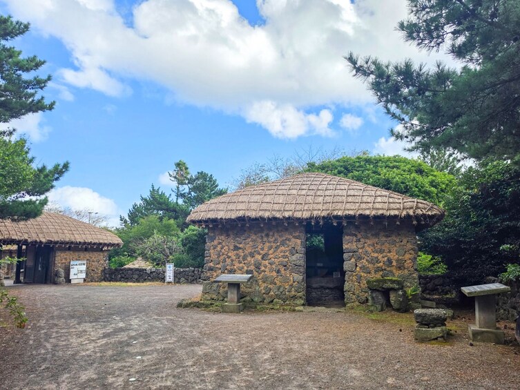 A traditional stone building with a thatched roof, surrounded by trees and a clear sky. 2