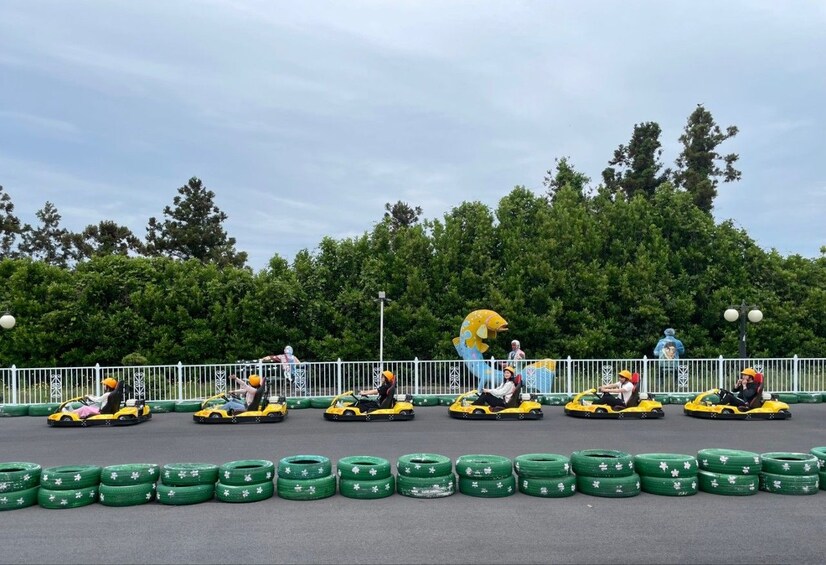 People driving go-karts on a track with green tires and a large fish decoration. 5