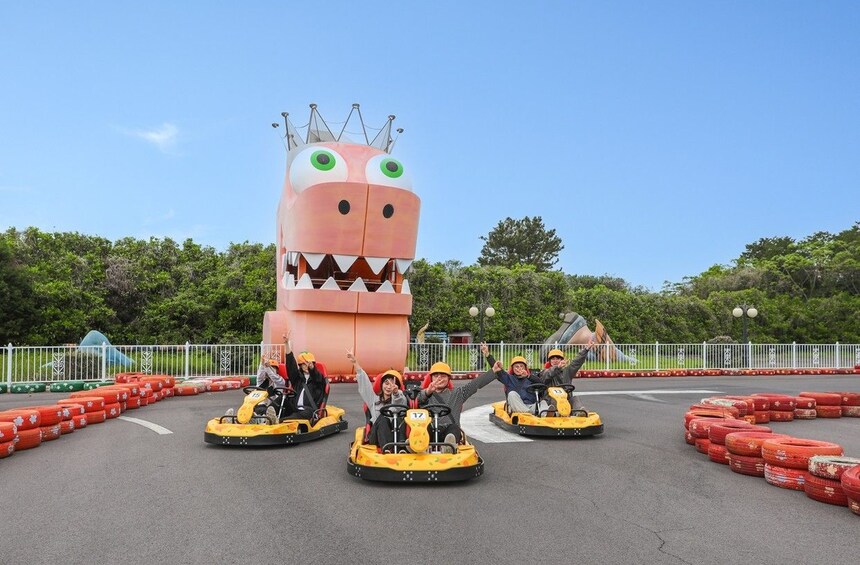 People riding bumper cars at an amusement park with a large pink monster decoration. 1