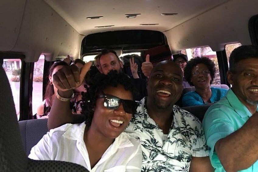 People inside a vehicle with a window, some wearing sunglasses and one person making a peace sign. 1