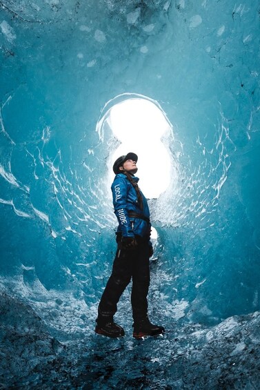 Una persona con una chaqueta azul parada en una cueva de hielo con una gran abertura en la parte superior. 2