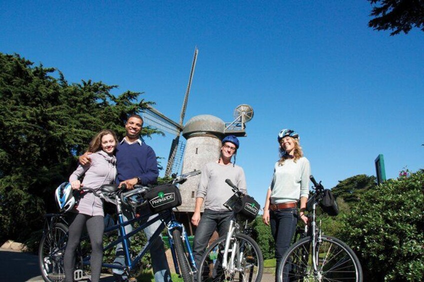A group of people with bicycles in front of a windmill. 1