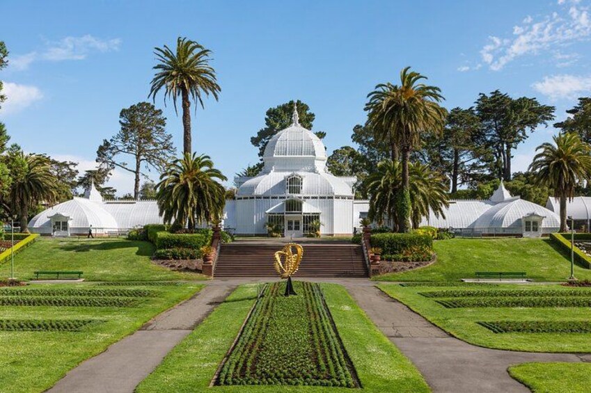 A botanical garden with a large greenhouse, palm trees, and well-manicured lawns. 4