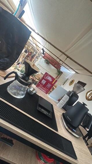 Een houten tafel met een zwart toetsenbord, een glazen waterkoker, een zwarte koffiezetapparaat en een rood bord met QR-codes op de achtergrond. 2