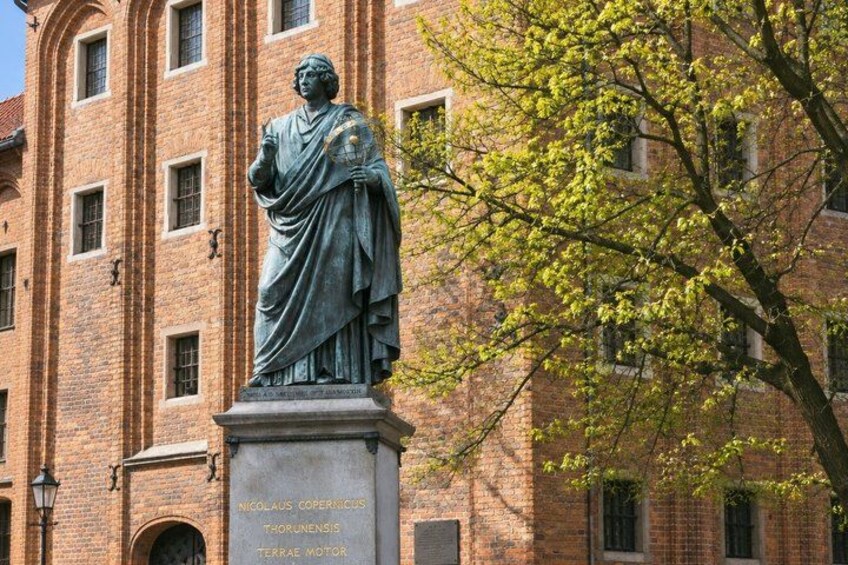 A statue of Nicolaus Copernicus in front of a brick building with arched windows. 4