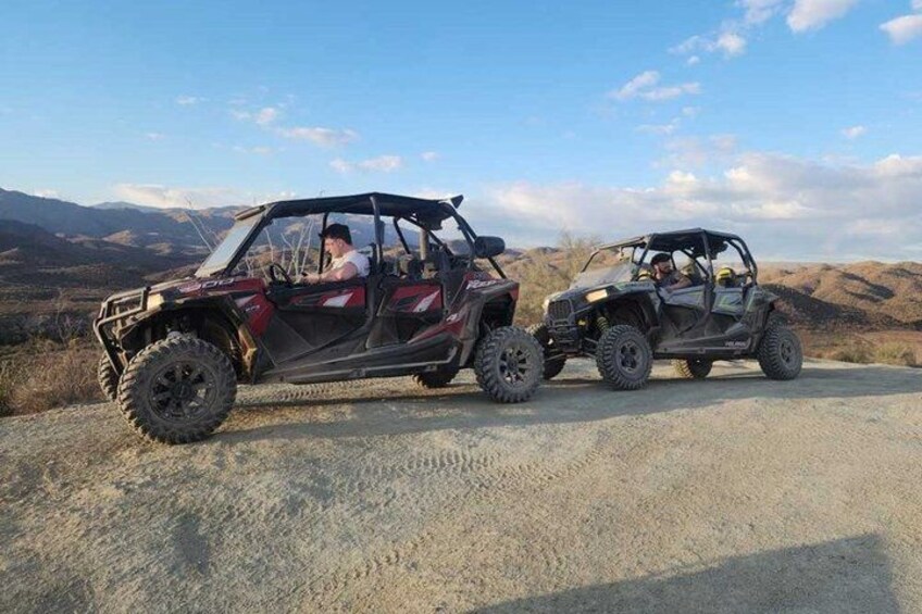 Two off-road vehicles on a dirt road with a mountainous landscape in the background. 4