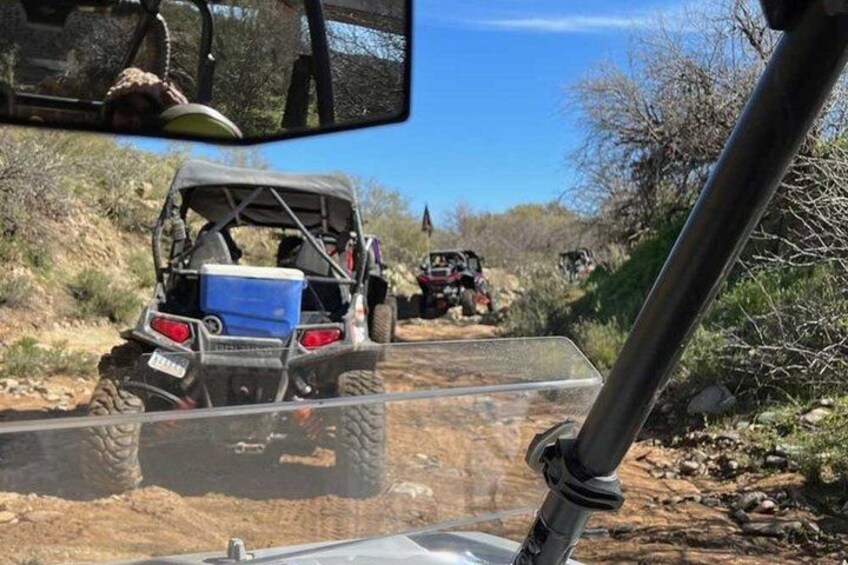 An off-road vehicle on a dirt path with a clear blue sky and sparse vegetation. 3