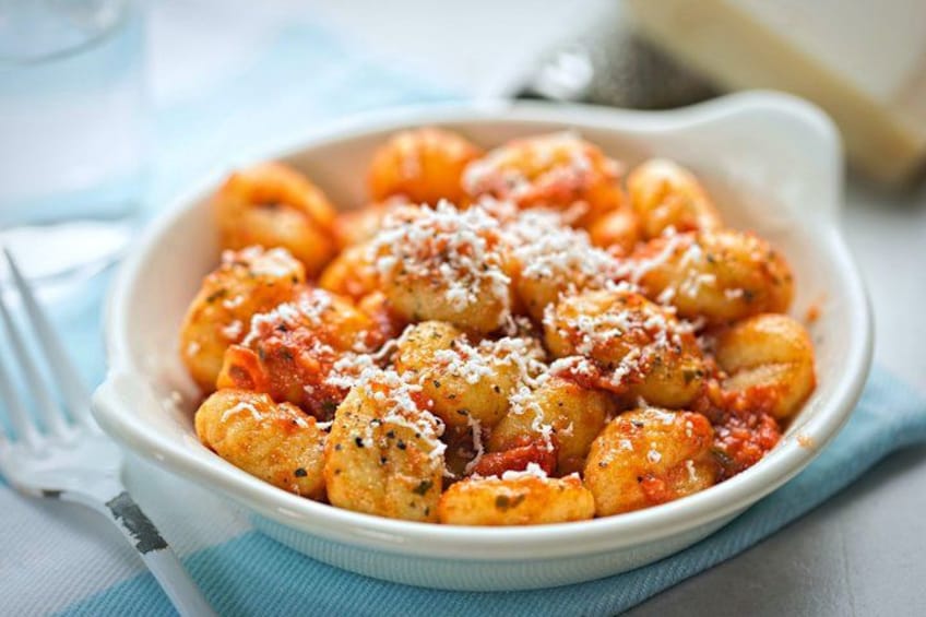 A bowl of gnocchi with tomato sauce and grated cheese. 5