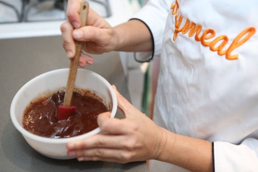 A person stirring a thick, dark mixture in a white bowl. 2
