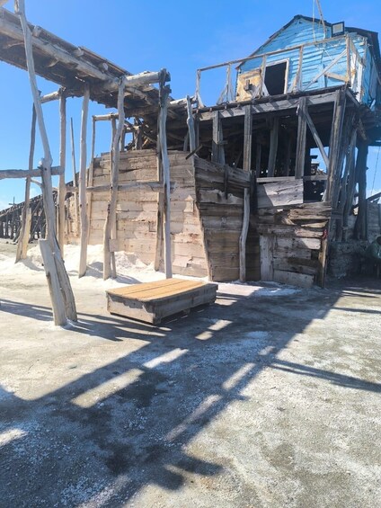 A dilapidated wooden structure with a blue roof, surrounded by snow. 5