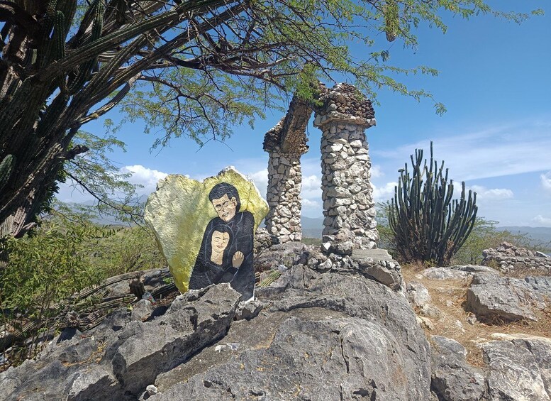 A rock formation with a painted mural, a stone structure, and a cactus in a desert landscape. 3