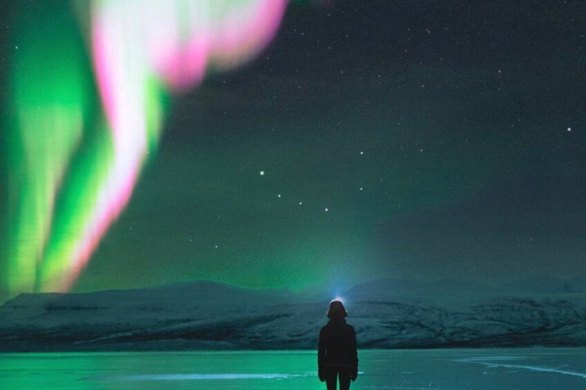 A person standing on a flat surface with a mountain range in the background and the aurora borealis in the sky. 4