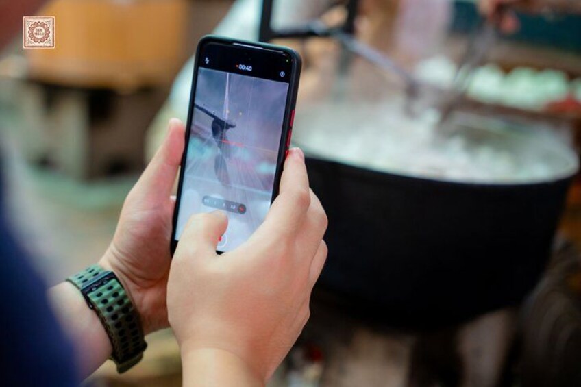 A person holding a smartphone with a cooking pot in the background. 3