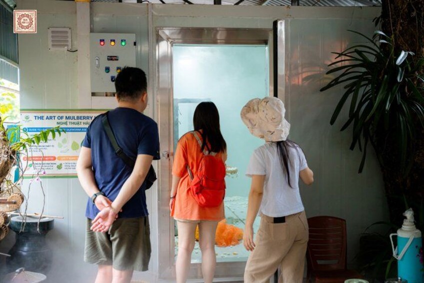 A group of people standing in front of a glass elevator door, with a sign about mulberry art visible in the background. 5