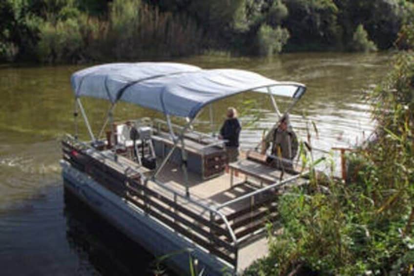 A boat with a canopy on a calm river surrounded by greenery. 1