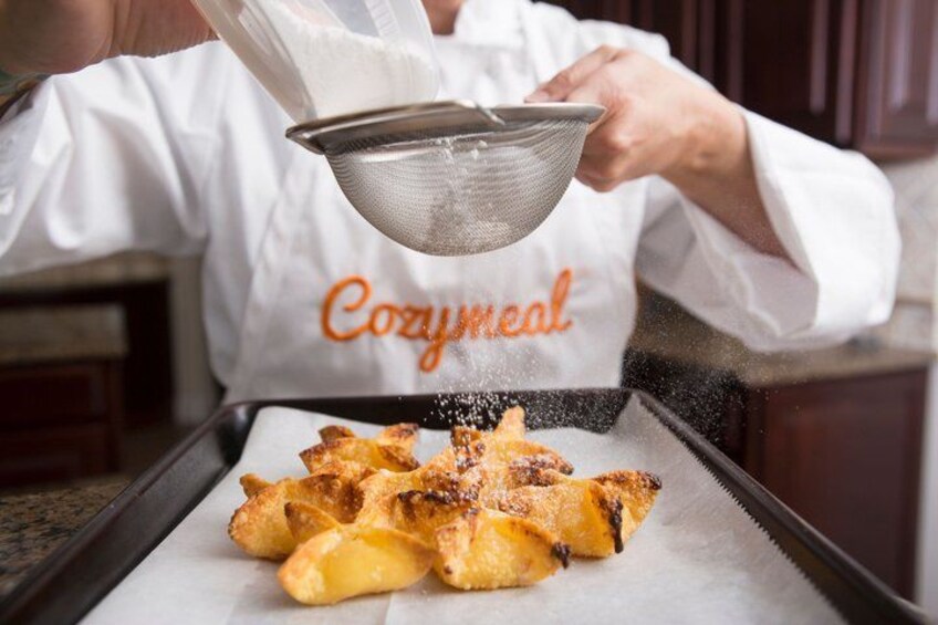 A person in a white chef's coat with 'Cozymmeal' text, sprinkling seasoning over roasted potatoes on a baking tray. 3