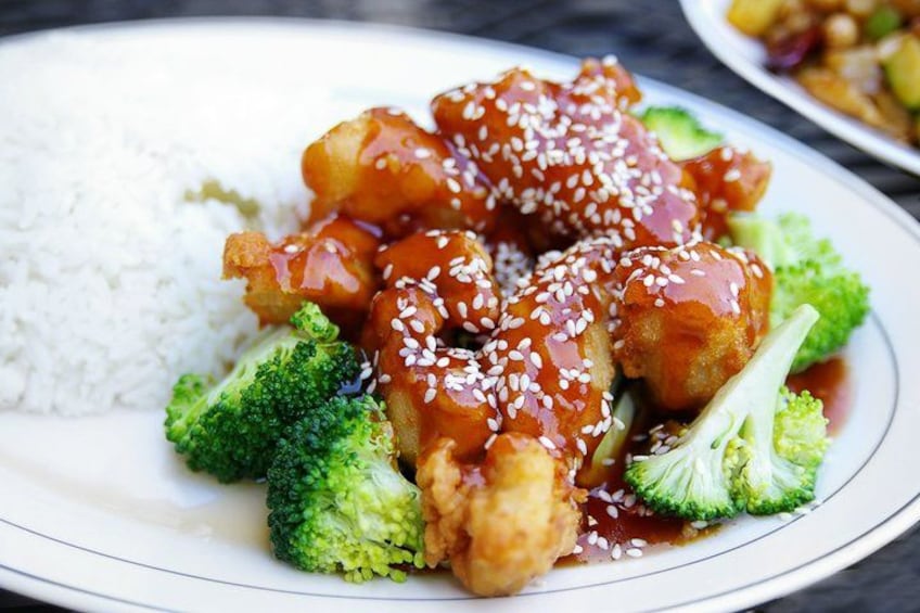A plate of food with sesame seed-topped chicken, broccoli, and white rice. 1