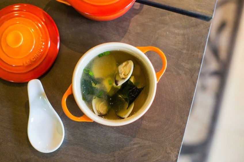 A bowl of soup with a lid and a ladle on a table. 5