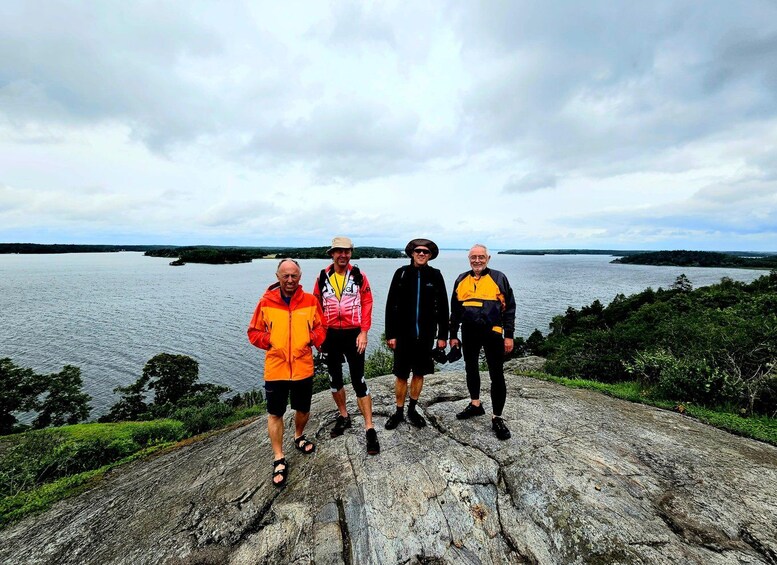 Four people standing on a rocky ledge overlooking a body of water. 4