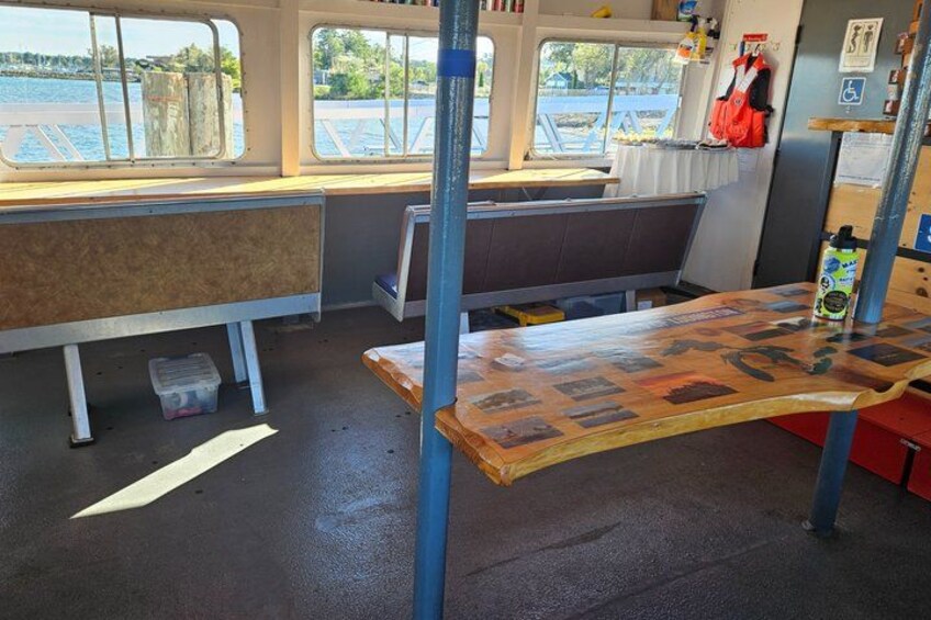A boat interior with a wooden table, benches, and windows overlooking water. 5