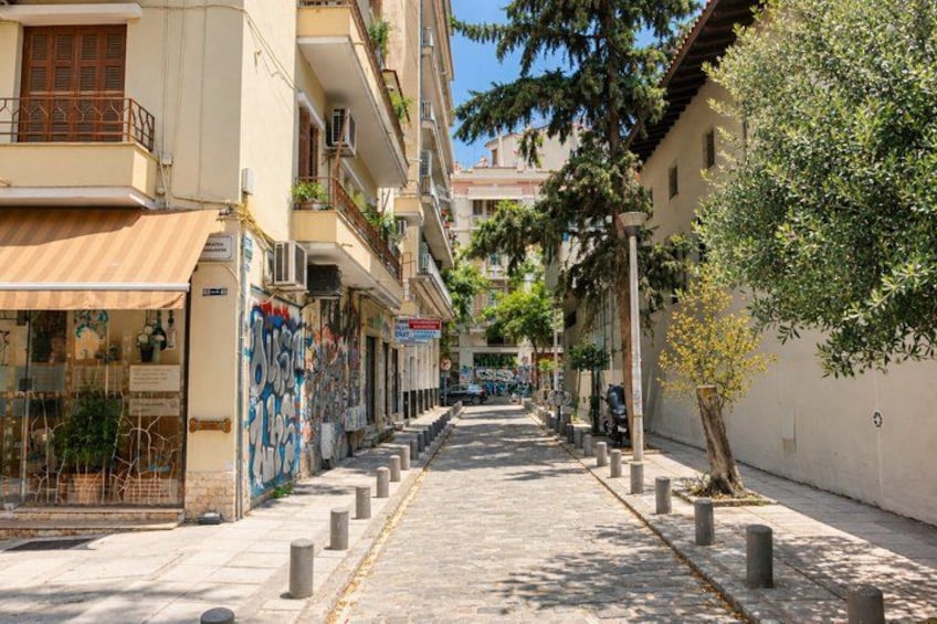 A narrow urban street lined with multi-story buildings, some with balconies and plants. 5