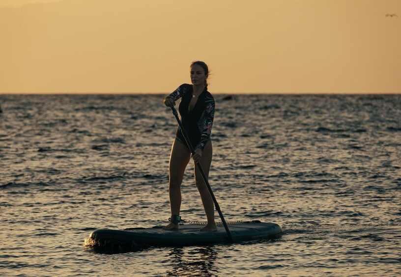 A person paddleboarding on a body of water during sunset. 5