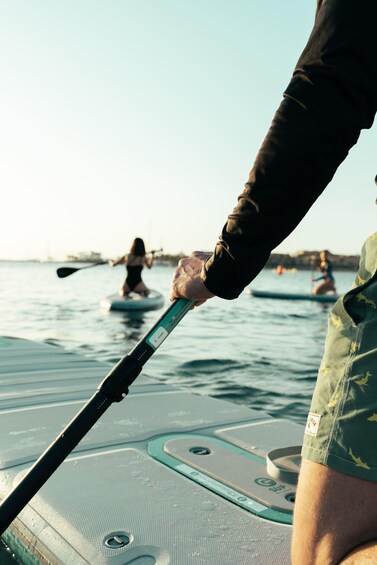 A person paddling on a paddleboard in a body of water with other paddleboarders in the background. 2