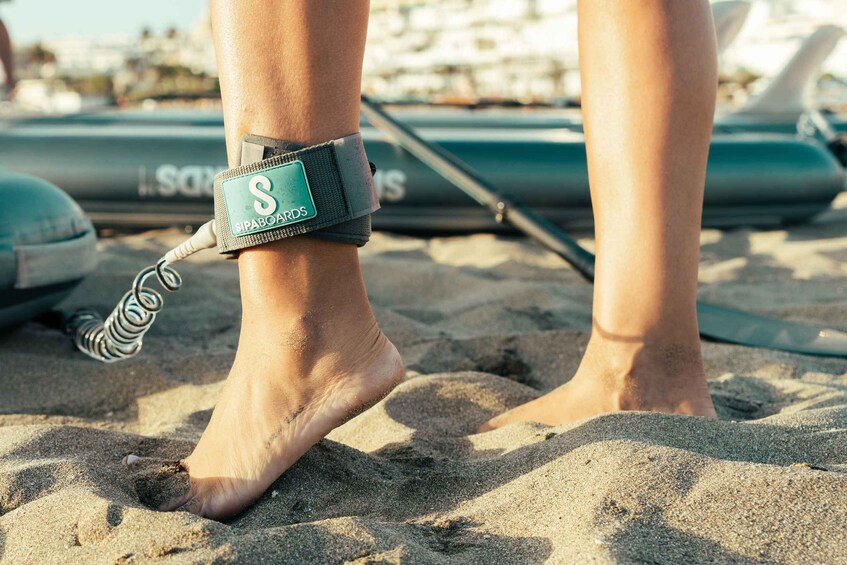 A person wearing a swim ankle strap on a sandy beach with a boat in the background. 4