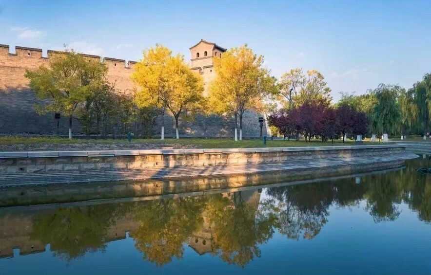 A calm river reflecting trees and a historic building. 1
