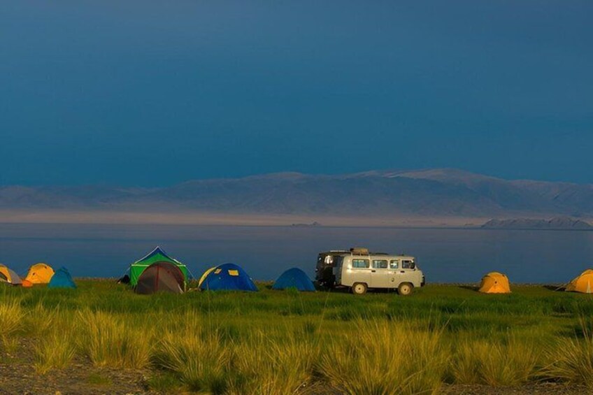 A white van parked among colorful tents in a grassy field with mountains in the background. 5