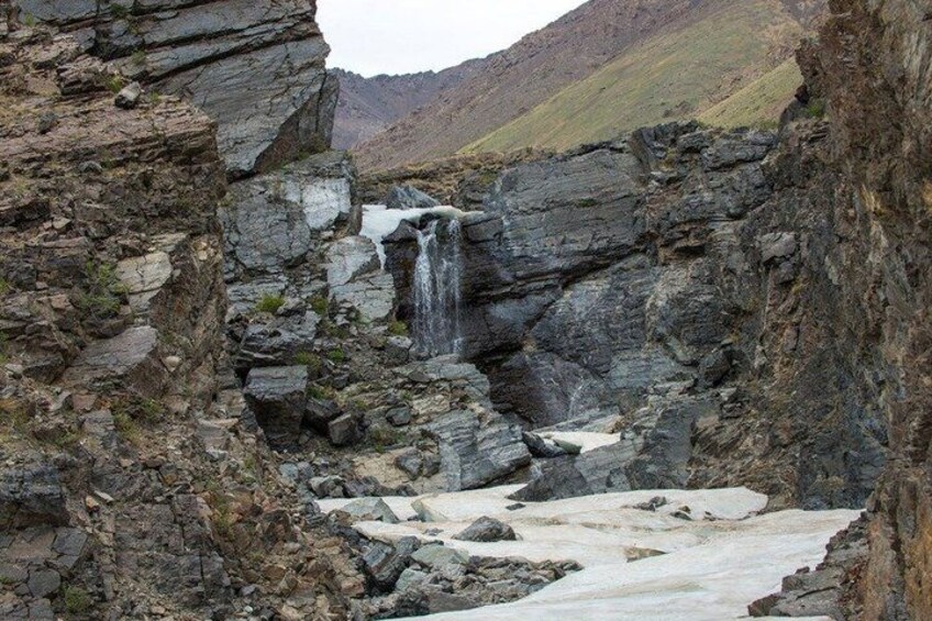 A waterfall cascading down a rocky cliff, surrounded by rugged terrain and a distant mountain. 4