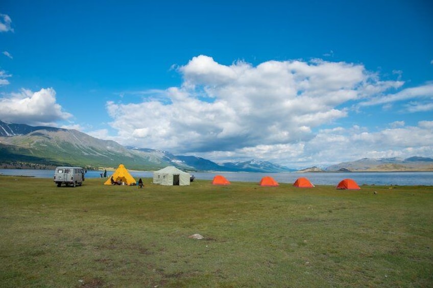 A grassy field with tents, a vehicle, and mountains in the background. 1