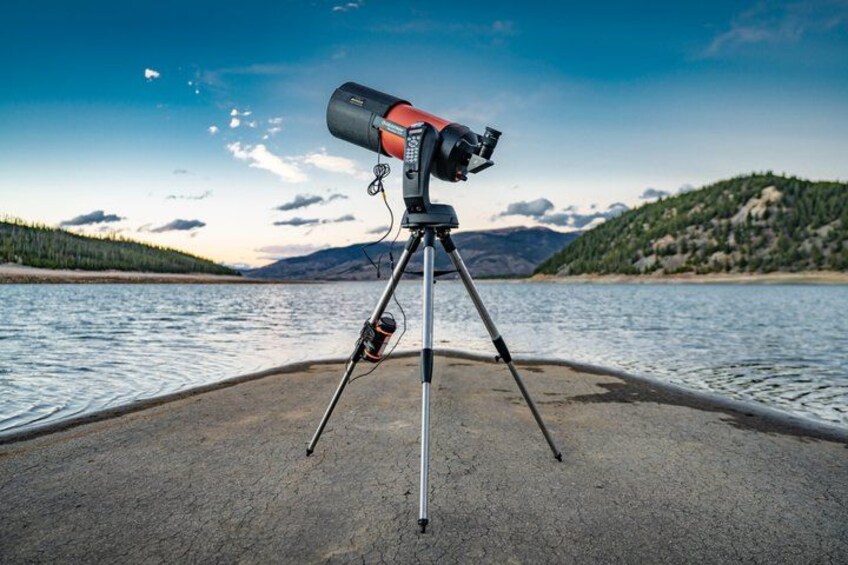A telescope on a tripod by a lake with mountains in the background. 2