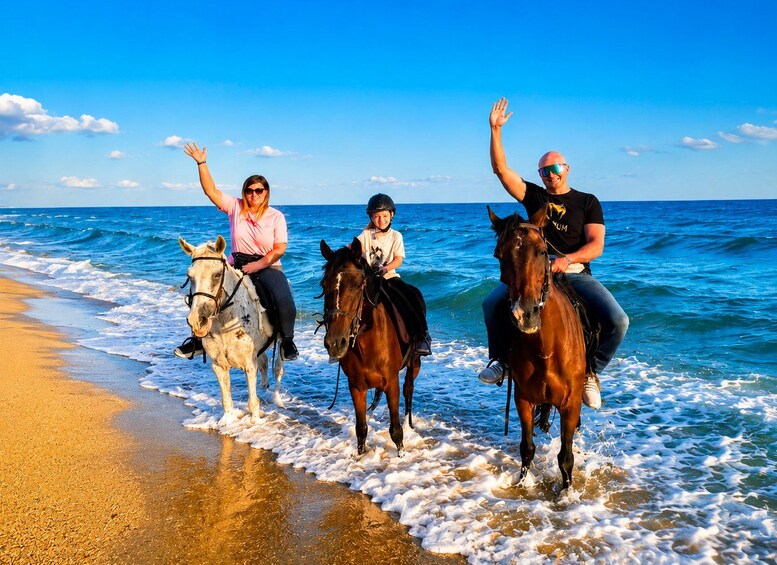 Three people riding horses along a beach with waves lapping at their feet. 5