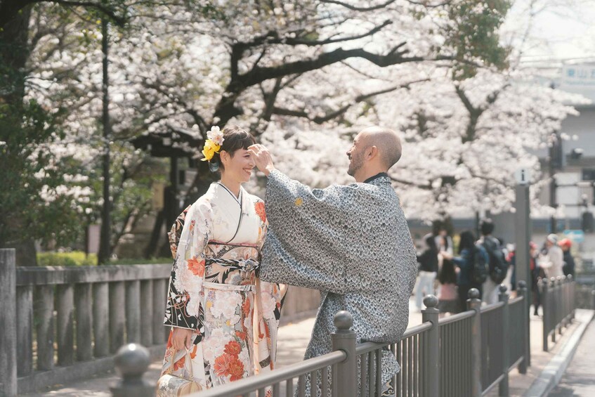 A person in traditional attire with a flower in their hair, standing on a bridge with cherry blossoms in the background. 4