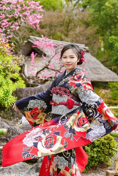 A person in traditional attire with a kimono, standing in a garden with cherry blossoms and a thatched-roof structure. 3