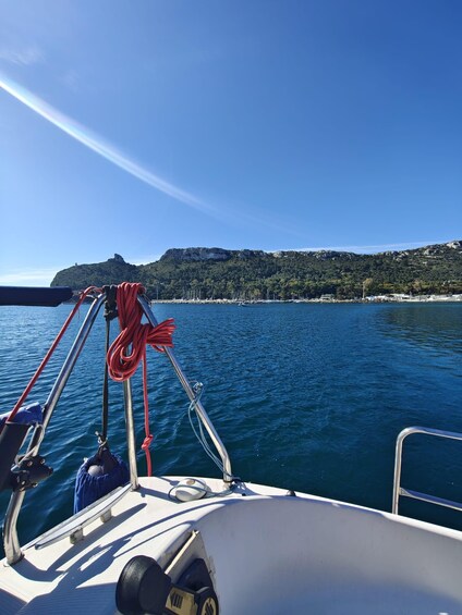 A boat's bow with ropes and metal railings, calm blue sea, and a coastline with a hill and buildings. 4