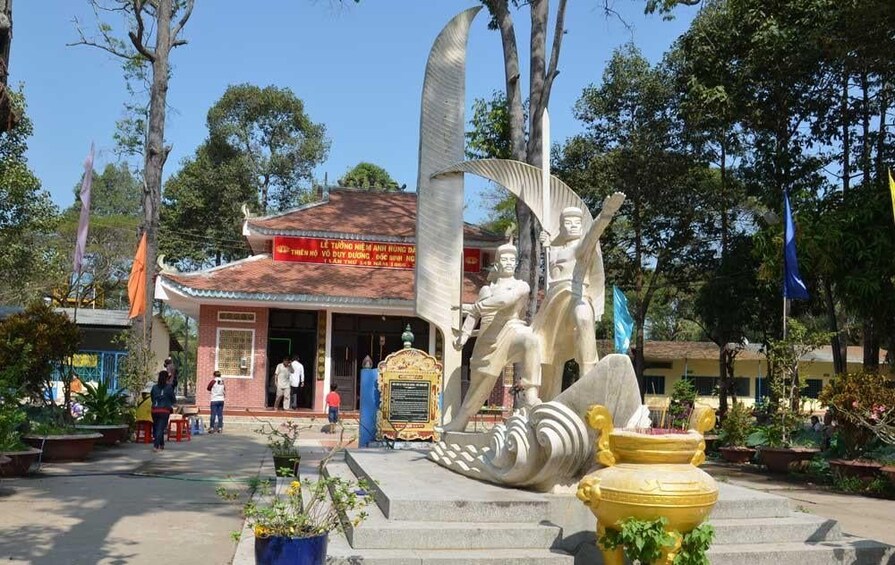 A temple with a large statue of a figure holding a sword, surrounded by trees and a yellow lotus pond. 5