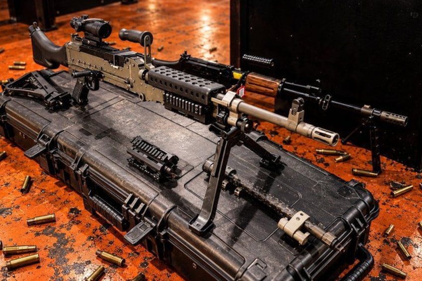 A large, custom-built firearm with a scope and bipod, surrounded by scattered bullets on a red floor. 3