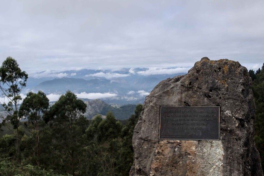 A mountain landscape with a plaque on a rock, trees, and a cloudy sky. 4
